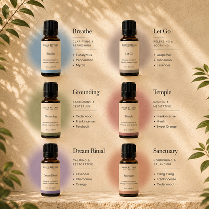 Six small amber glass essential oil bottles from Daily Ritual Cosmetics arranged in a 3x2 grid on a warm beige textured background with decorative leaf shadows. Each bottle is labeled with a different scent name: Breathe, Let Go, Grounding, Temple, Dream Ritual, and Sanctuary.