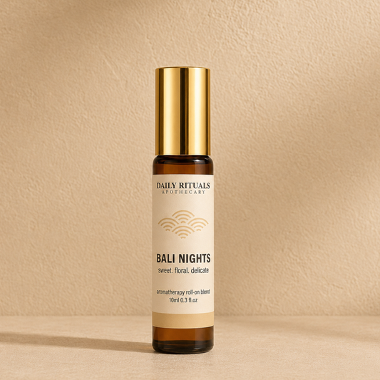 A 10ml roll-on bottle of Bali Nights aromatherapy oil by Daily Rituals Apothecary, featuring a gold cap and cream-colored label on an amber glass bottle, set against a textured beige background.