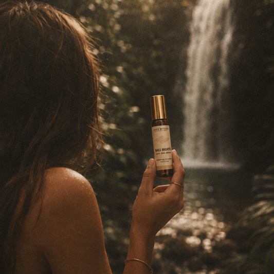 A woman in a forest setting with a waterfall in the background holds up a bottle of 'Sage & Root' 'Bile Modifier' supplement. The image has a warm, golden-hour filter with a soft-focus background.